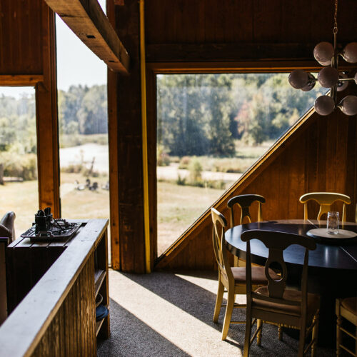 An interior view of the wood-paneled rental unit with geometric windows, a modern light fixture, and a dining table at Verdant Hollow Farm in Buchanan, Michigan.