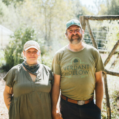Farm managers Molly and Brett Muchow holding hands and standing in front of a wooden fence at Verdant Hollow Farm in Buchanan, Michigan.