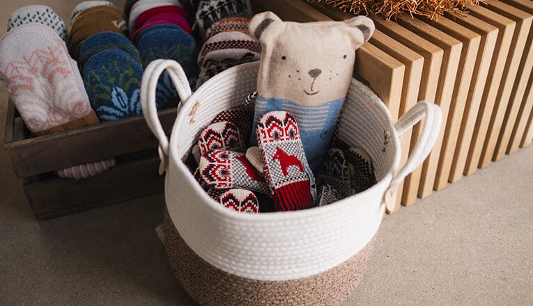 A basket filled with Öjbro Vantfabrik wool mittens and a bear stuffed animal sit inside Stockholm Objects in Harbert, Michigan