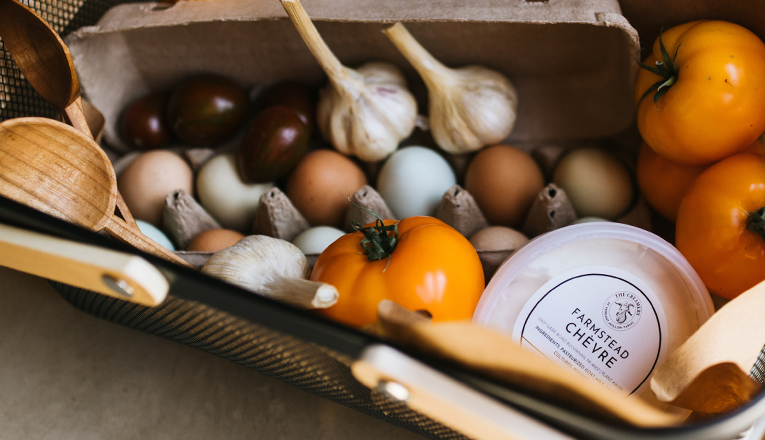A market basket full of eggs, garlic, tomatoes, handrafted wooden spoons, and farmstead cheese at Verdant Hollow Farms in Buchanan, Michigan.