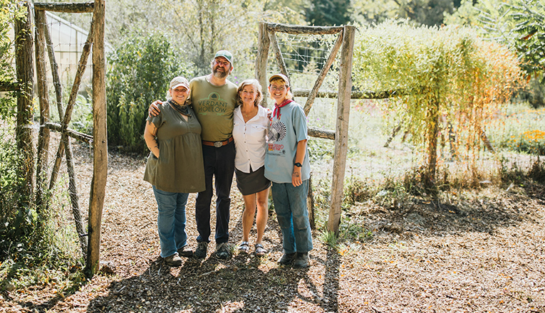 The Verdant Hollow famrs team stands at the opening of a rustic wooden garden gate.