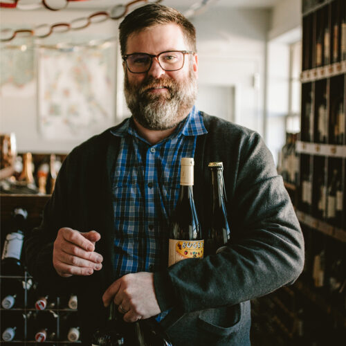 Pat Mullins smiling carrying bottles of wine at P&E Bottle Shop in Three Oaks, Michigan