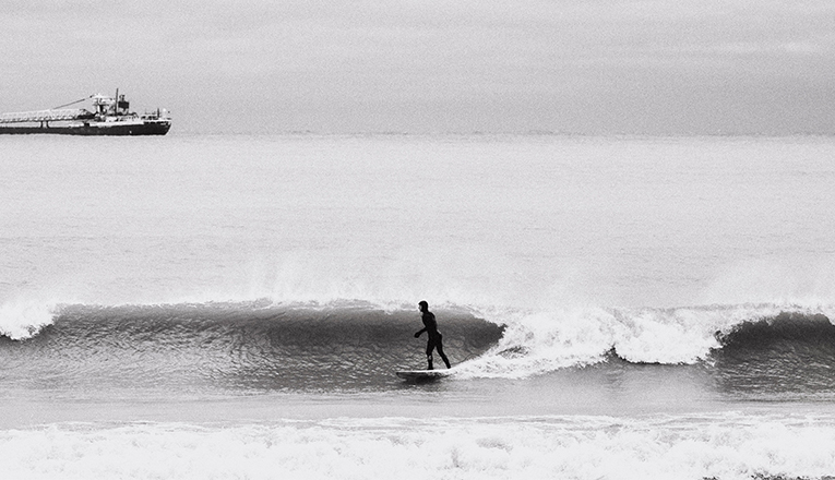 A surfer surfing in Lake Michigan in winter, a cargo ship sailed past in the background