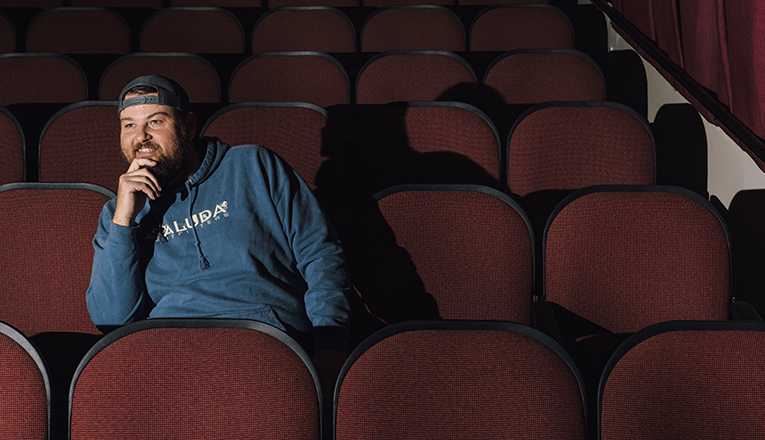 Zach Hackett, Vickers Theatre's newest owner sits in a movie seat and smiles.