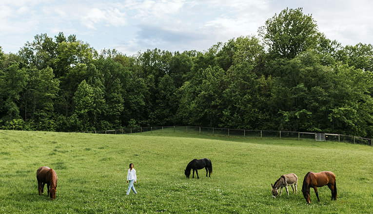 Elizabeth Carden walks through a field with horses at Inner Freedom in Buchanan, Michigan