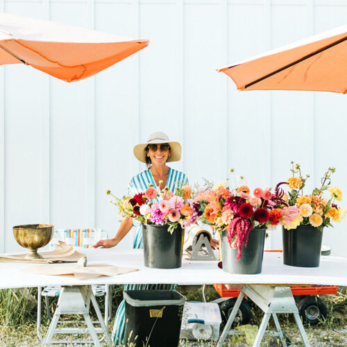 A woman stands behind buckets of freshly cut flowers from Homecamp Flower Farm in Three Oaks, Michigan
