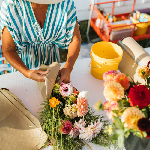 A woman assembles a fresh flower bouquet on a table with brown paper at Homecamp Flower Farm in Three Oaks, Michigan