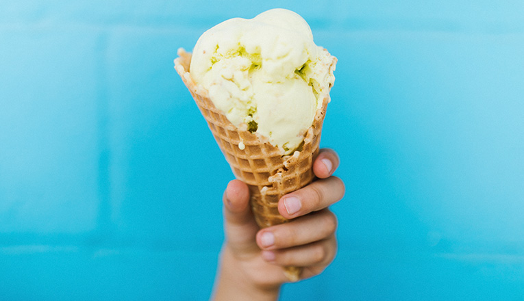 A hand holding a waffle cone with a scoop of ice cream at The Beach Bucket in Sawyer, Michigan
