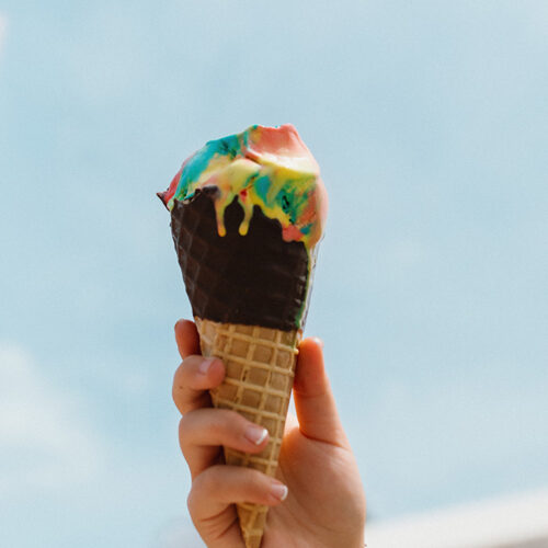 A hand holds up a rainbow ice cream cone at Oinks Dutch Treat in New Buffalo, Michigan